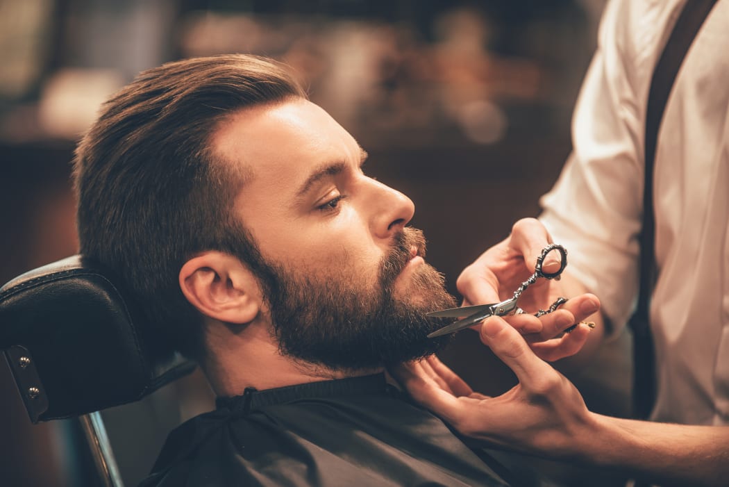 Close-up side view of young bearded man getting beard at barber shop.