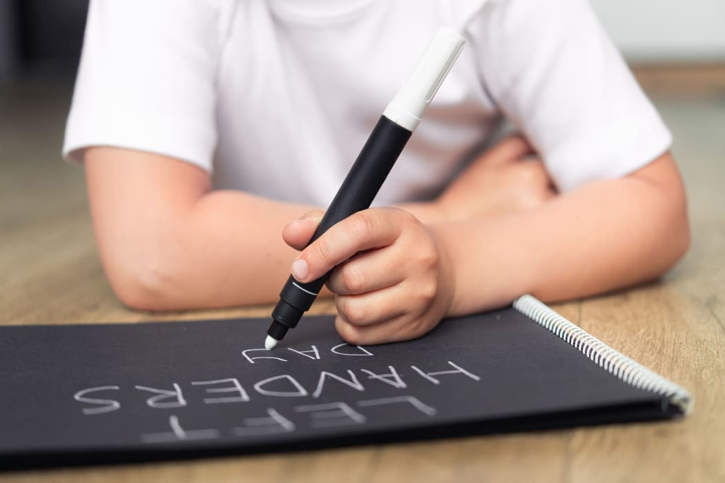 Left-handed child with a marker writes words on a notebook.