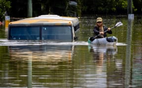 A man paddles his kayak next to a submerged bus on a flooded street in the town of Milton in suburban Brisbane on February 28, 2022.