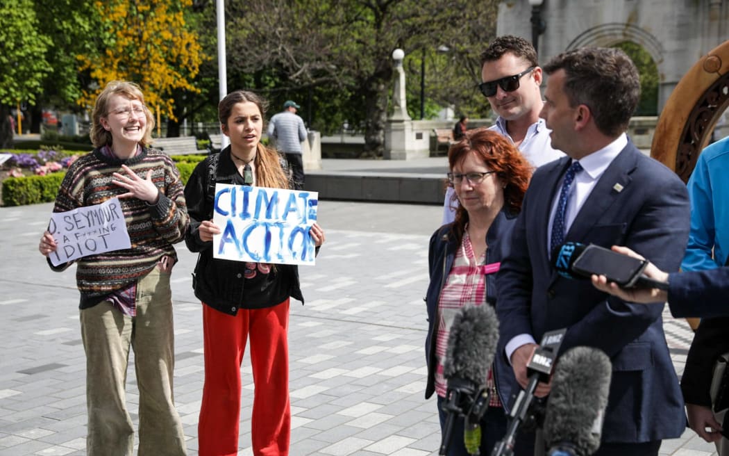 ACT leader David Seymour speaks to media with two teenage protesters standing behind him on 10 October, 2023