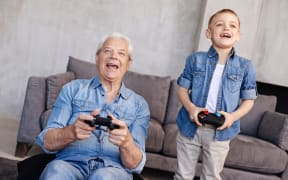 A photo of a boy teaching his father or grandfather how to game using a gaming controllers.