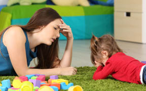 A photo of a frustrated crying baby and a tired mother with some toy blocks lying near them
