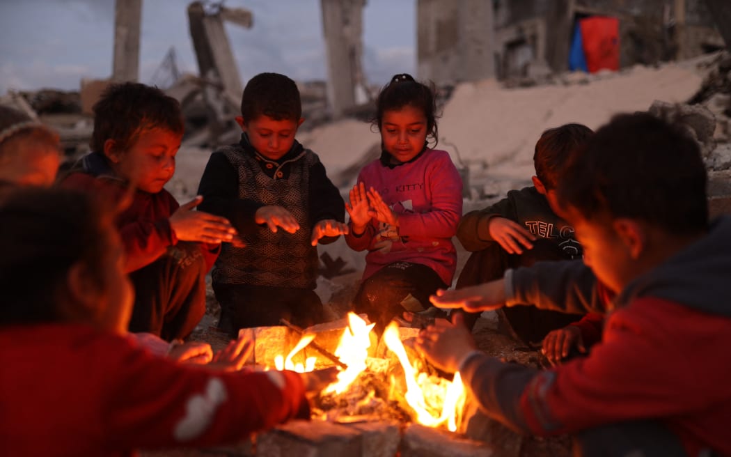 Displaced Palestinians warm up by the fire after their homes are destroyed following heavy rain in Gaza City, Palestine, on January 14, 2026.