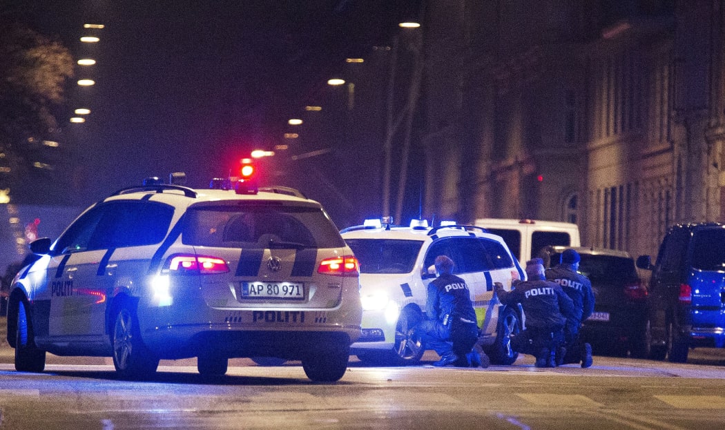 Police officers take cover behind their patrol cars after one person was shot in the head and two policemen were shot in the arm and leg in Krystalgade.