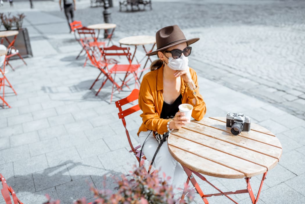 Young woman in facial mask sitting on the cafe terrace alone. Concept of social distancing and new social rules after coronavirus pandemic.