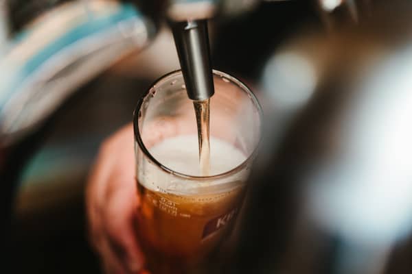A person's hand can be seen holding a beer glass as the beer pours from a tap in a bar.