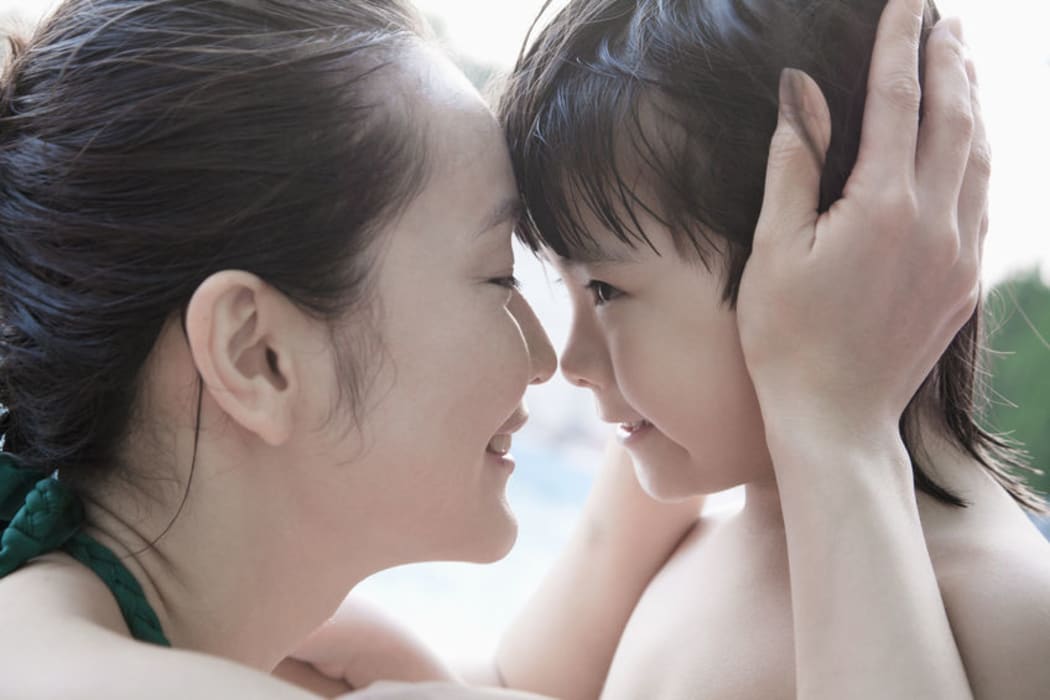 A photo of a smiling mother and son embracing and holding head by the pool