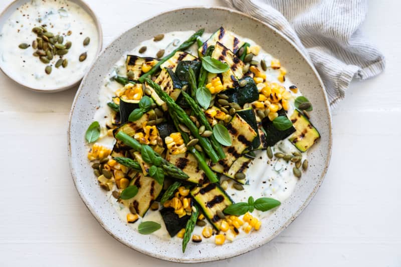 A round platter containing arbecued courgette and sweetcorn salad with basil yoghurt dressing, garnished with pumpkin seeds.