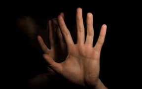 Man putting up hands to hide face (almost obscured in background)