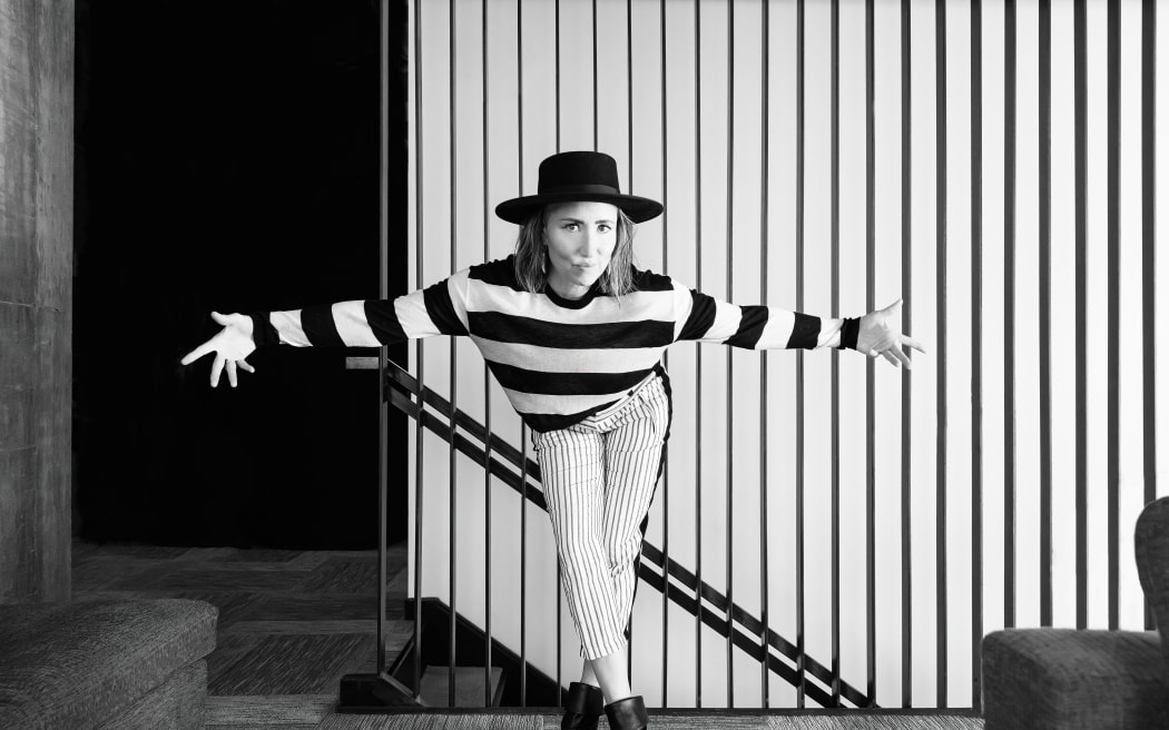 A black and white photo of singer songwriter KT Tunstall wearing stripey clothing, bowing in front of a striped wall.