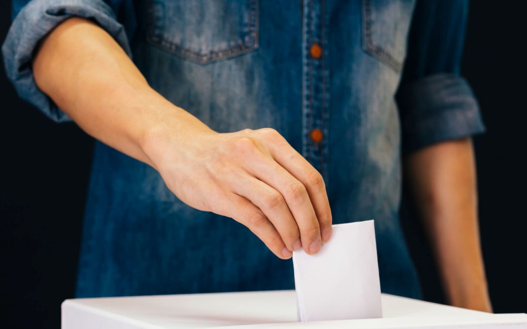 Front view of person holding ballot paper casting vote at a polling station for election vote in black background