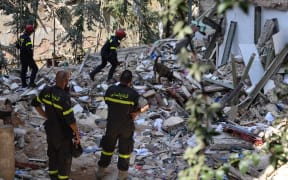 Members of the Lebanese civil defence look on as French rescuers use a dog to search for victims and survivors amidst the rubble of a building in the Gemayzeh neighbourhood on August 6, 2020, two days after a massive explosion in the Beirut port shook the capital.