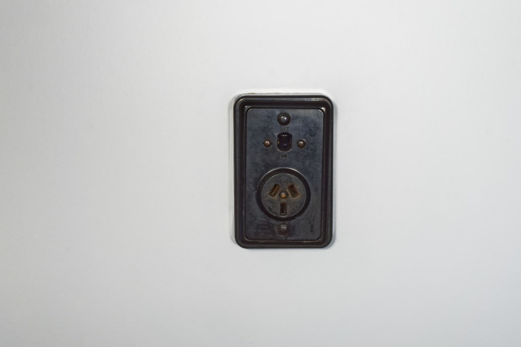 Old fashioned bakelite power socket with on/off switch on a white plaster wall