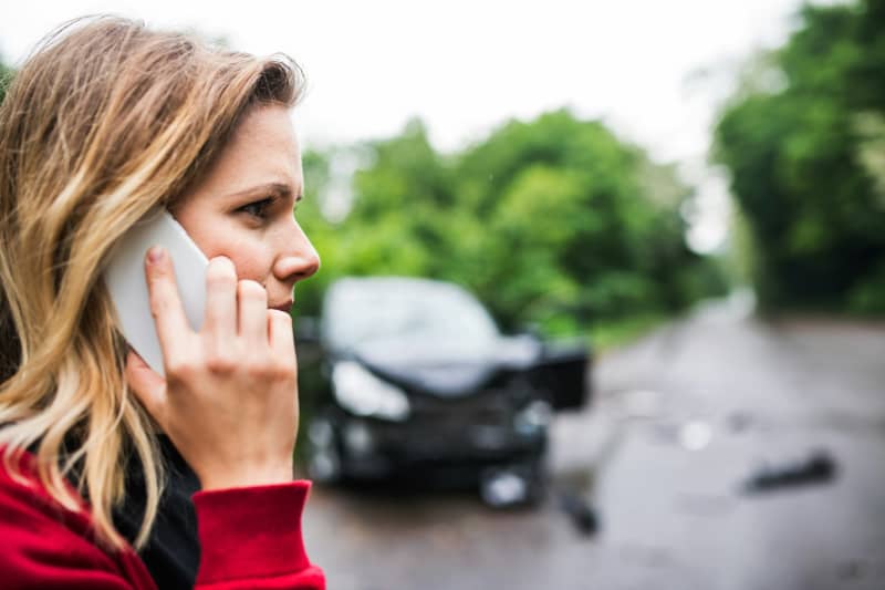 A woman on a mobile phone at the scene of a car accident.
