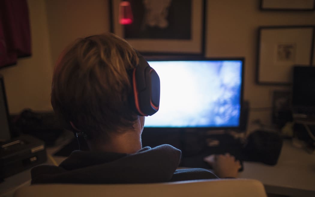 Teenage boy with headphones playing video game in dark bedroom. (Photo by CAIA IMAGE/SCIENCE PHOTO LIBRARY / NEW / Science Photo Library via AFP)
