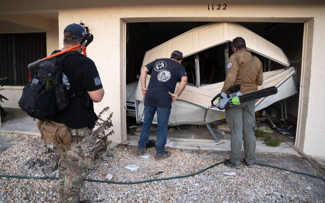 SANIBEL ISLAND, FL - OCTOBER 01: Bryan Stern, right, Dean Calderone, and Alexander Toal, left, of the Project DYNAMO rescue organization, look into a garage in the wake of Hurricane Ian on October 1, 2022 on Sanibel Island, Florida. Known for rescues in Afghanistan and Ukraine, the Florida based Project DYNAMO team was unable to make contact with the person they were searching for on this mission.   Sean Rayford/Getty Images/AFP (Photo by Sean Rayford / GETTY IMAGES NORTH AMERICA / Getty Images via AFP)