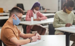 Side view portrait of young man wearing mask while taking test or exam in school with diverse group of people, copy space