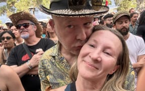 A man in a hat kisses the cheek of a woman with long blonde hair.