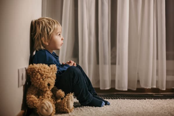 Sad child sitting in corner with teddy bear.