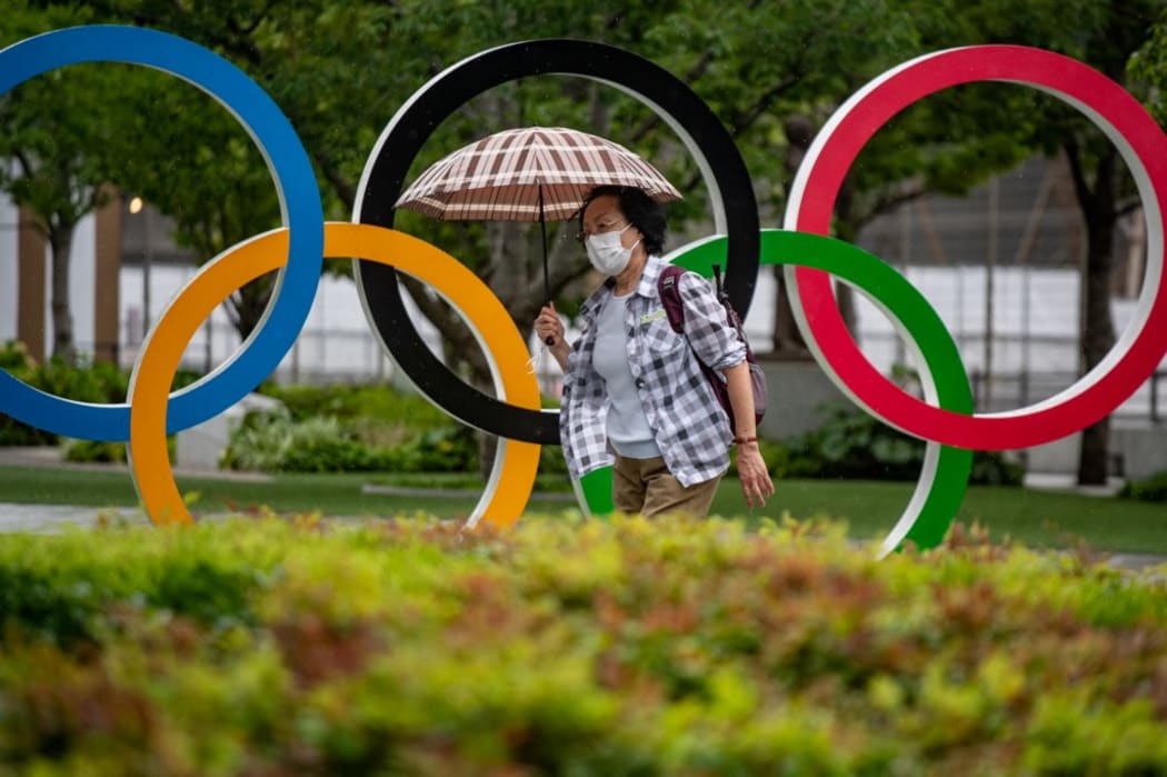 A woman holds an umbrella walking past the Olympic Rings in front of Japan Olympic Museum in Tokyo on July 8, 2021. (Photo by Philip FONG / AFP)