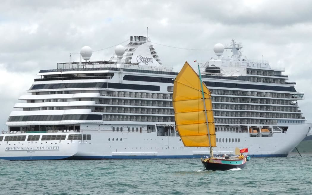 The junk rig FanShi, built and skippered by Annie Hill, is dwarfed by the Seven Seas Explorer.