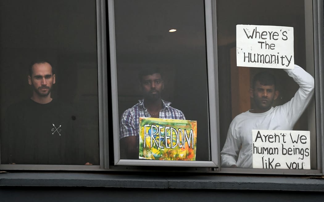 Three asylum seekers gesture to protesters holding a pro-refugee rights rally from their hotel room where they have been detained in Melbourne on June 13, 2020, after they were evacuated to Australia for medical reasons from offshore detention centres on Nauru and Manus Island. (Photo by William WEST / AFP)