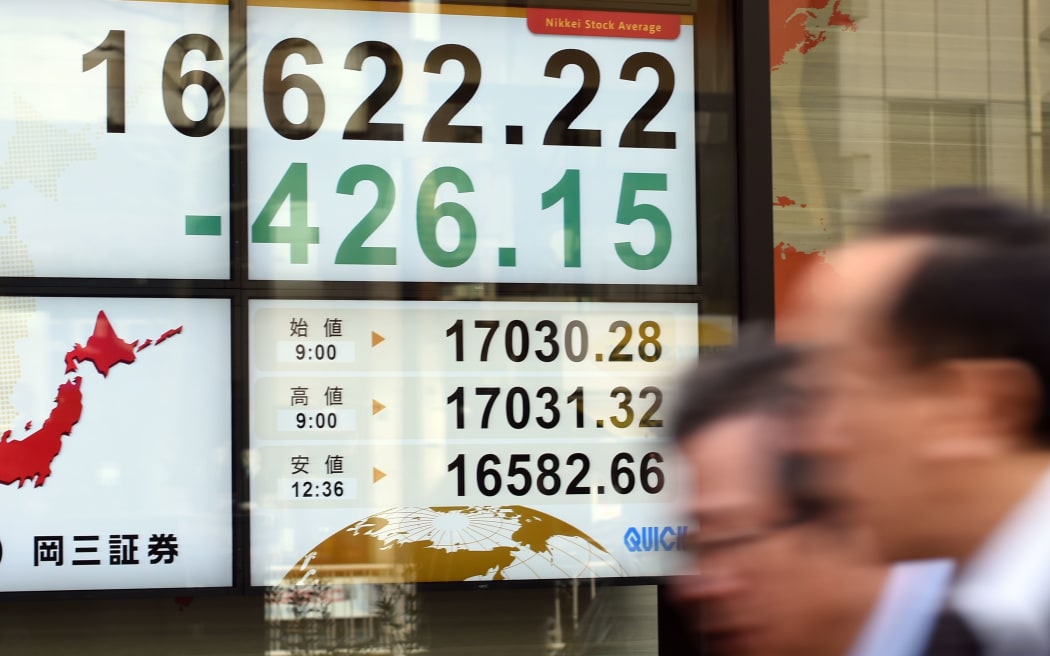 Businessmen walk past the stock indicator flashing Tokyo stock prices during its afternoon session in Tokyo on January 20, 2016.