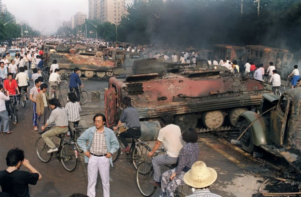 A file photo taken on 4 June, 1989 shows Beijing residents gathering around the smoking remains of over 20 armoured personnel carriers burnt by demonstrators during clashes with soldiers near Tiananmen Square.