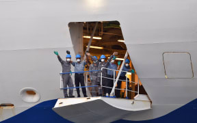 Crew members from the cruise ship Ruby Princess wave as they depart from Port Kembla, some 80 kilometres south of Sydney, on April 23, 2020, after a few hundred virus-free crew members disembarked to begin the process of repatriation to their home countries. -