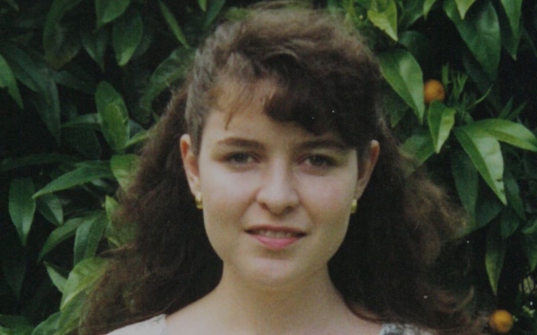 An image of Rachel Lees in her early 20s, she has long brown hair and is wearing a floral dress while standing in front of a fruit tree.