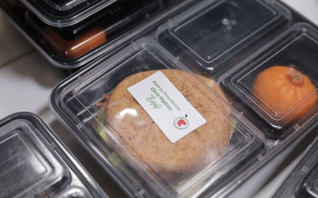 Chris Hipkins is visiting the Post Office Hotel in Pahiatua. They make free school lunches for approx 900 students in the area. Hipkins is helping make burgers which will be delivered to schools later.