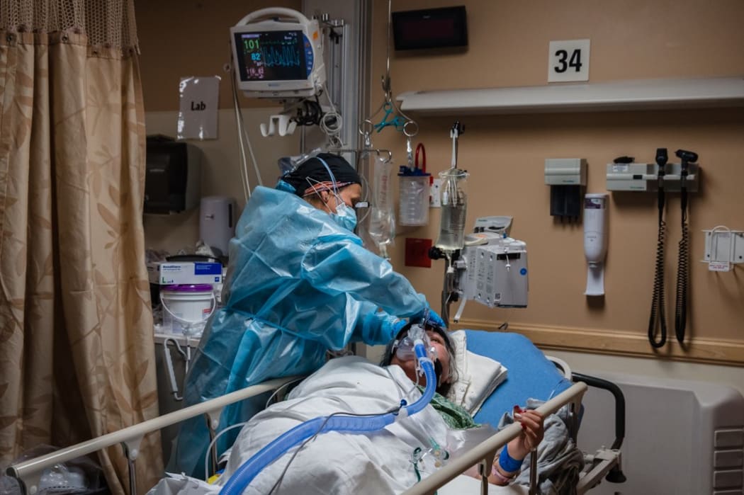 A health care worker tends to a Covid-19 patient while she is using a continuous positive airway pressure (CPAP) machine to help with her breathing difficulties in a Covid-19 holding pod at Providence St. Mary Medical Center in Apple Valley, California on January 11, 2021.