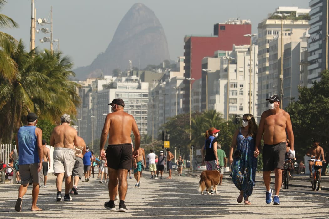 People walk along the edge of Copacabana beach in Rio de Janeiro, Brazil. The country's Covid-19 death toll has surpassed Italy.