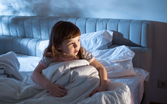 A photo of a girl of 4 years at night time who looks afraid to go to sleep