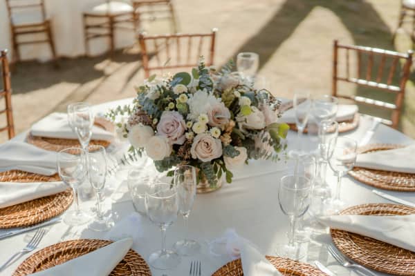 Flower bouquet on a round table set with linen, plates and wine glasses.