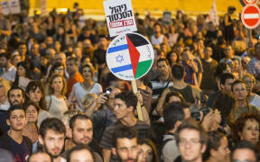 An Israeli left-wing activist holds a banner bearing images of the Israeli and Palestinian flags during a rally demanding fresh Israeli-Palestinian peace talks