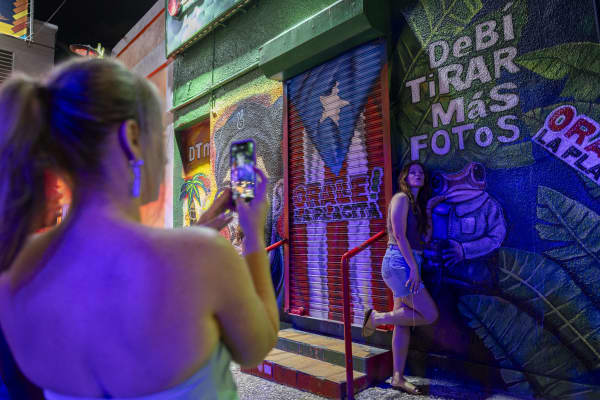 A woman poses in front of a mural at La Placita de Santurce in San Juan, Puerto Rico on July 12, 2025. The day before Bad Bunny kicked off his blockbuster residency that's expected to bring hundreds of millions of dollars to the island while showcasing its rich culture, he posted a simple message: Shop Local. The ethos is core to his 30-show concert series in San Juan which, after nine performaces exclusive to residents, will open up to fans from elsewhere -- what many Boricuas, as Puerto Ricans are known, are hoping will serve as an exercise in responsible tourism.