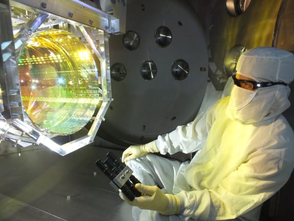 Prior to sealing up the chamber and pumping the vacuum system down, a LIGO optics technician inspects one of mirrors by illuminating its surface with light.