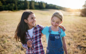 Two young girls with arms around each other, smiling.
