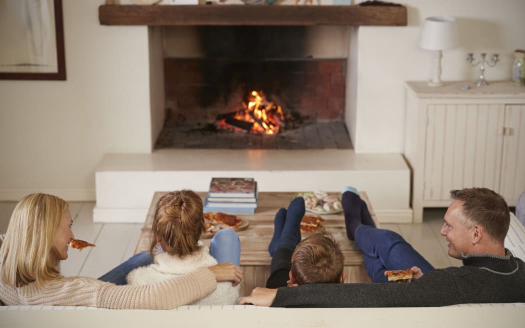 Family Sitting On Sofa In Lounge Next To Open Fire