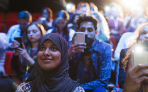 Smiling woman in hijab listening in audience.