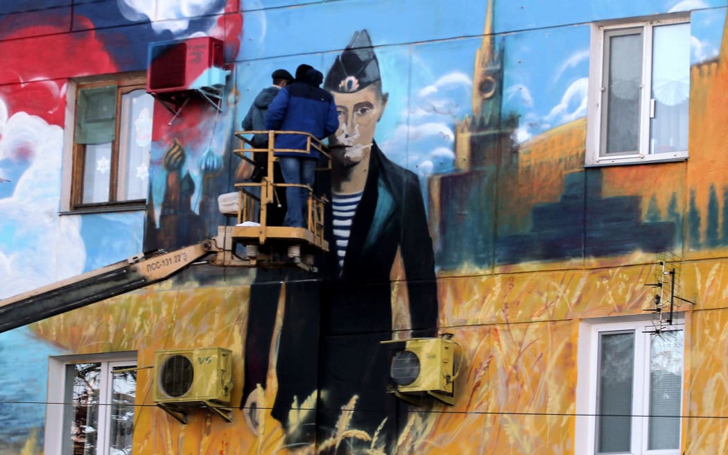 Workers on a crane in front of a mural depicting Vladimir Putin in a navy uniform, the Kremlin and the Russian flag on the wall of a building in the Crimean city, Sevastopol.