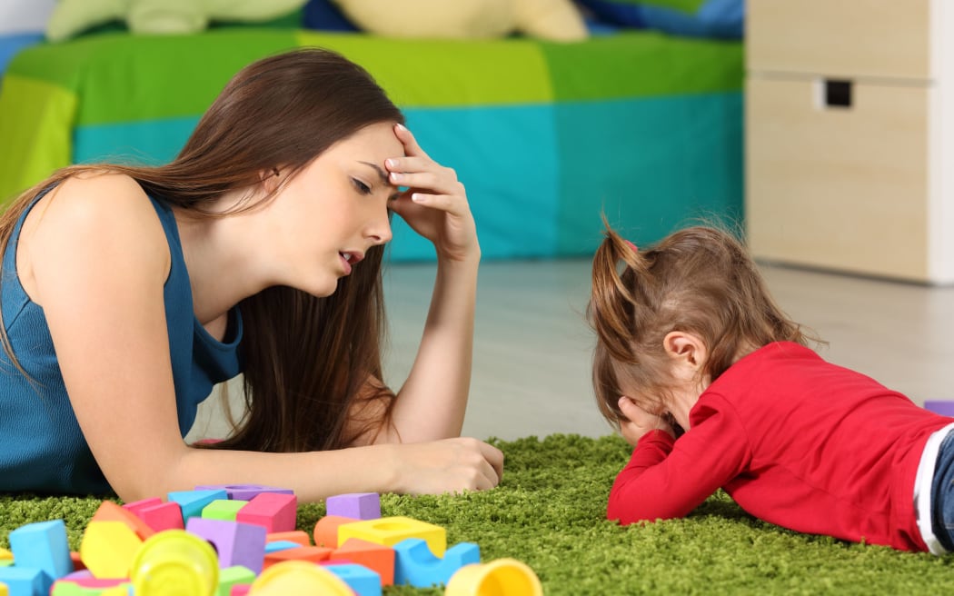A photo of a frustrated crying baby and a tired mother with some toy blocks lying near them