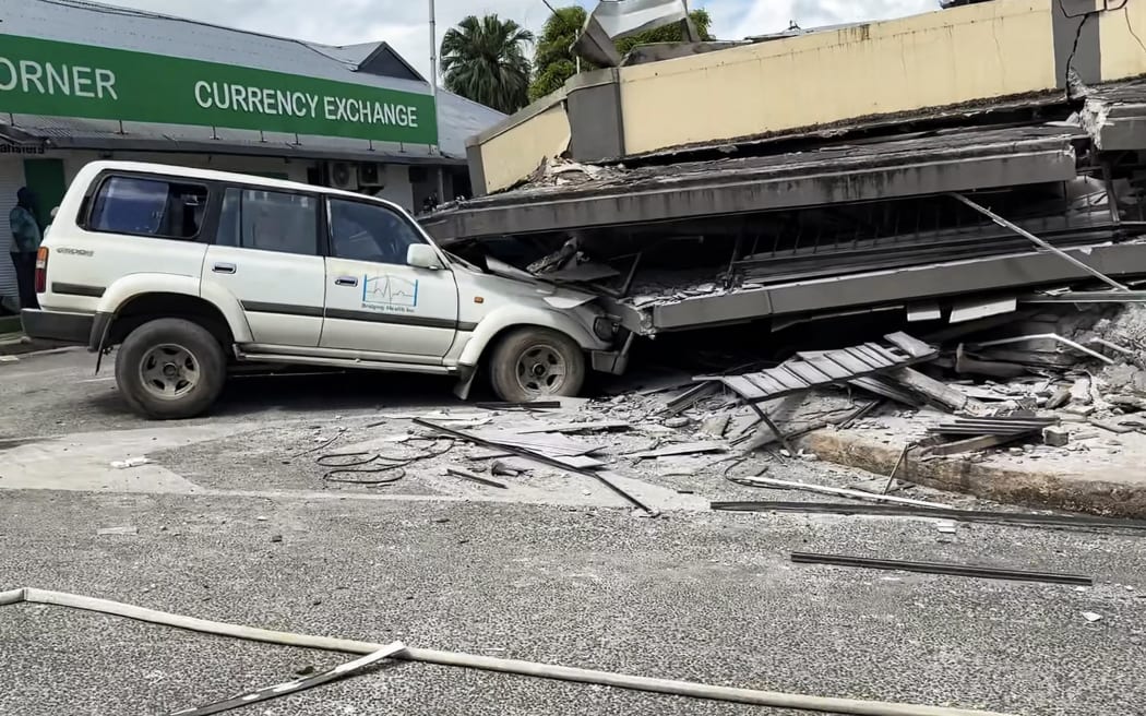 This screengrab taken from handout video footage posted on the Facebook account of Michael Thompson on 17 December, 2024 shows people inspecting a damaged car trapped underneath a collapsed building in Vanuatu's capital Port Vila after a powerful earthquake hit the Pacific island.