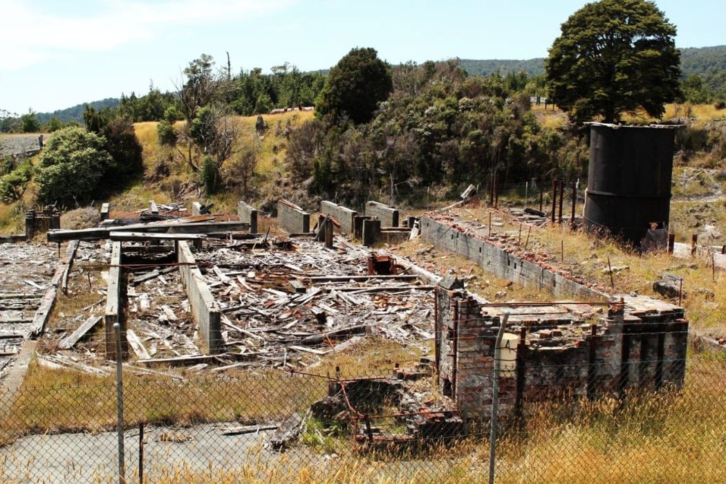 The remains of a demolished red brick building at Prohibition Mine in Waiuta, surrounded by grass and shrubs. The former mine on the West Coast is rated as the most toxic site in New Zealand