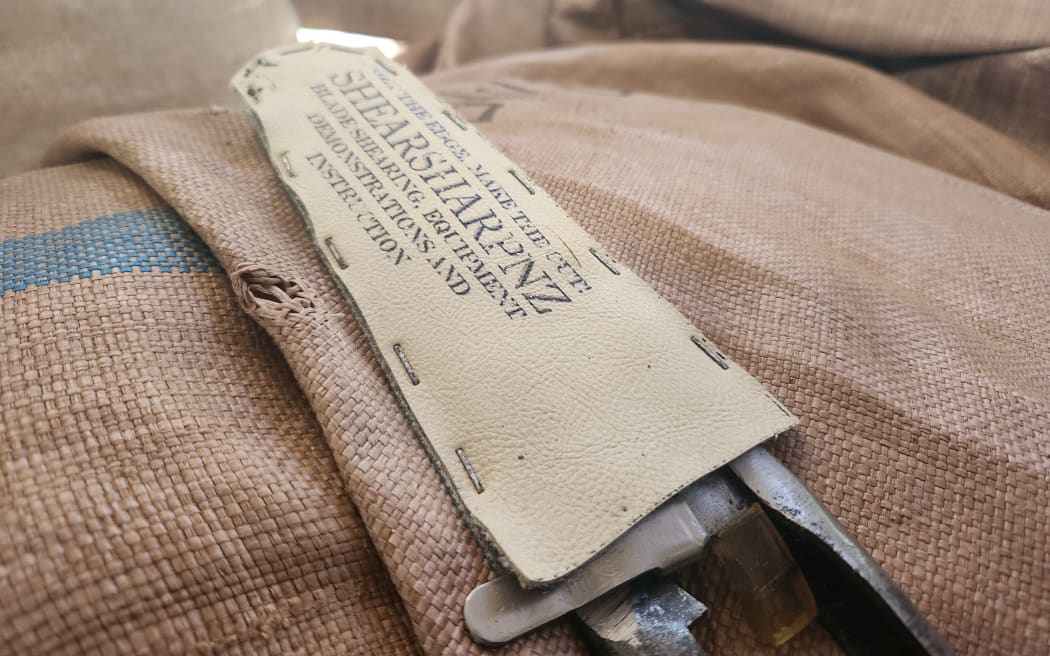 A close-up of a sheath holding a pair of blades. The sheath has the label Shear Sharp NZ, Allan Oldfield's shearing school.
