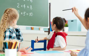 Elementary school kids sitting in classroom and looking at blackboard with multiplication sums