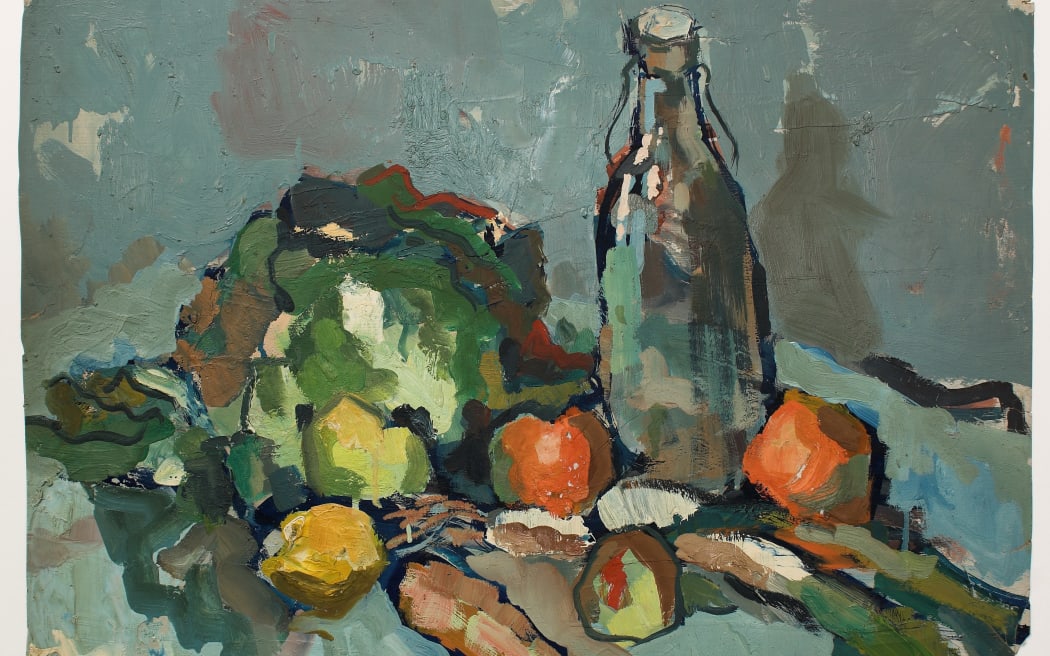 A still life. A handful of vegetables, a lettuce, lemon, carrot and tomatoes, next to a glass serving bottle of water.