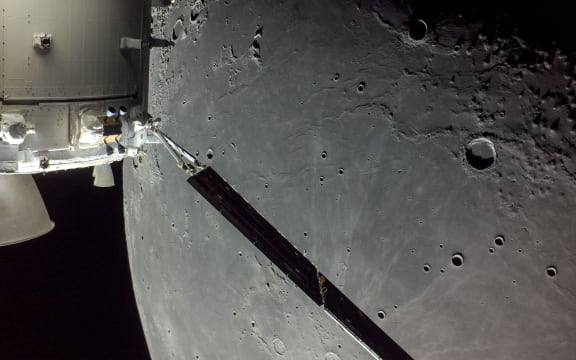 portion of the far side of the Moon looms large just beyond the Orion spacecraft in this image taken on the 20th day of the Artemis I mission by a camera on the tip of one of Orion’s solar arrays.