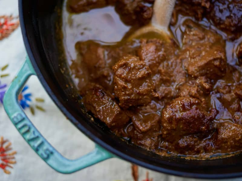 Fesenjān - a sweet and sour chicken stew from Northern Iran - is served in a black bowl with a wooden spoon.